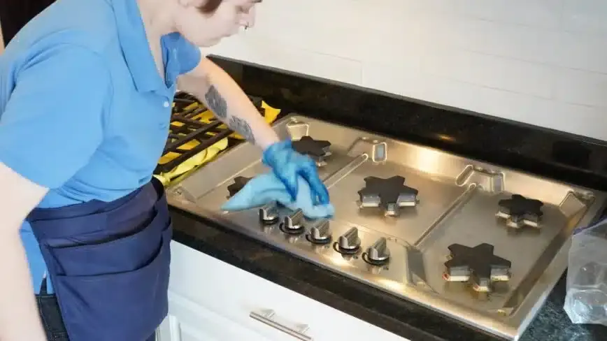 A cleaner in a blue Touch of Europe polo polishing a stainless gas cooktop with a cloth