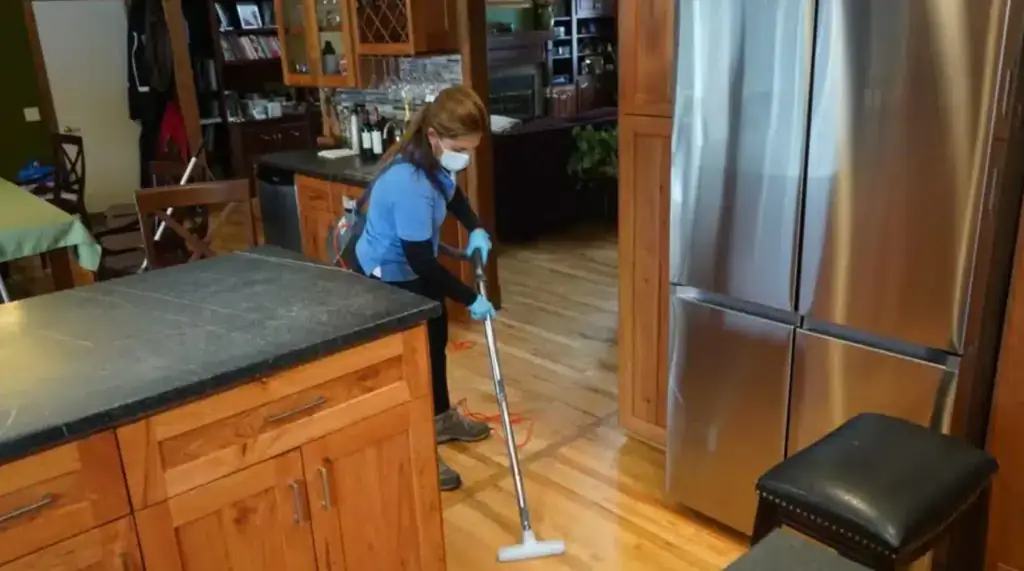A Touch of Europe cleaner mopping a wood kitchen floor beside a stainless refrigerator