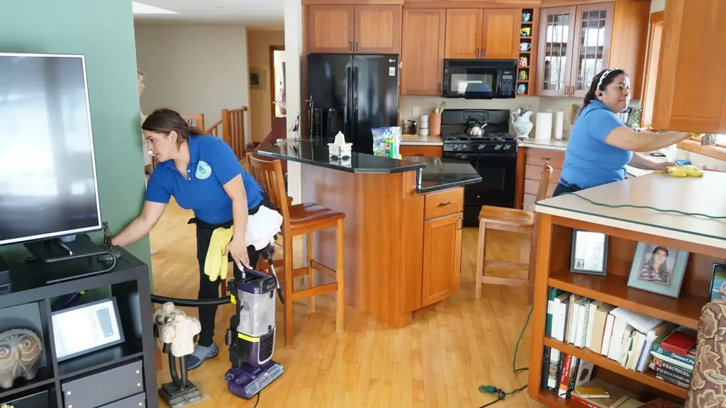 Two Touch of Europe cleaners at work, one dusting a TV stand, one wiping a kitchen counter