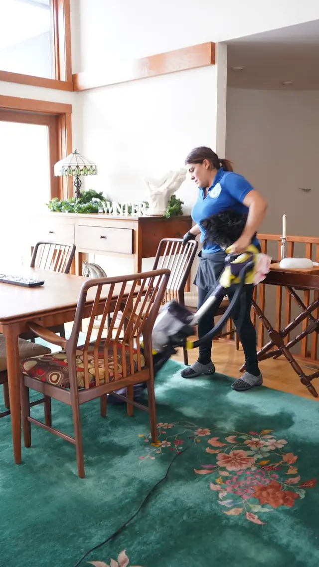 A cleaner vacuuming a rug in a dining room